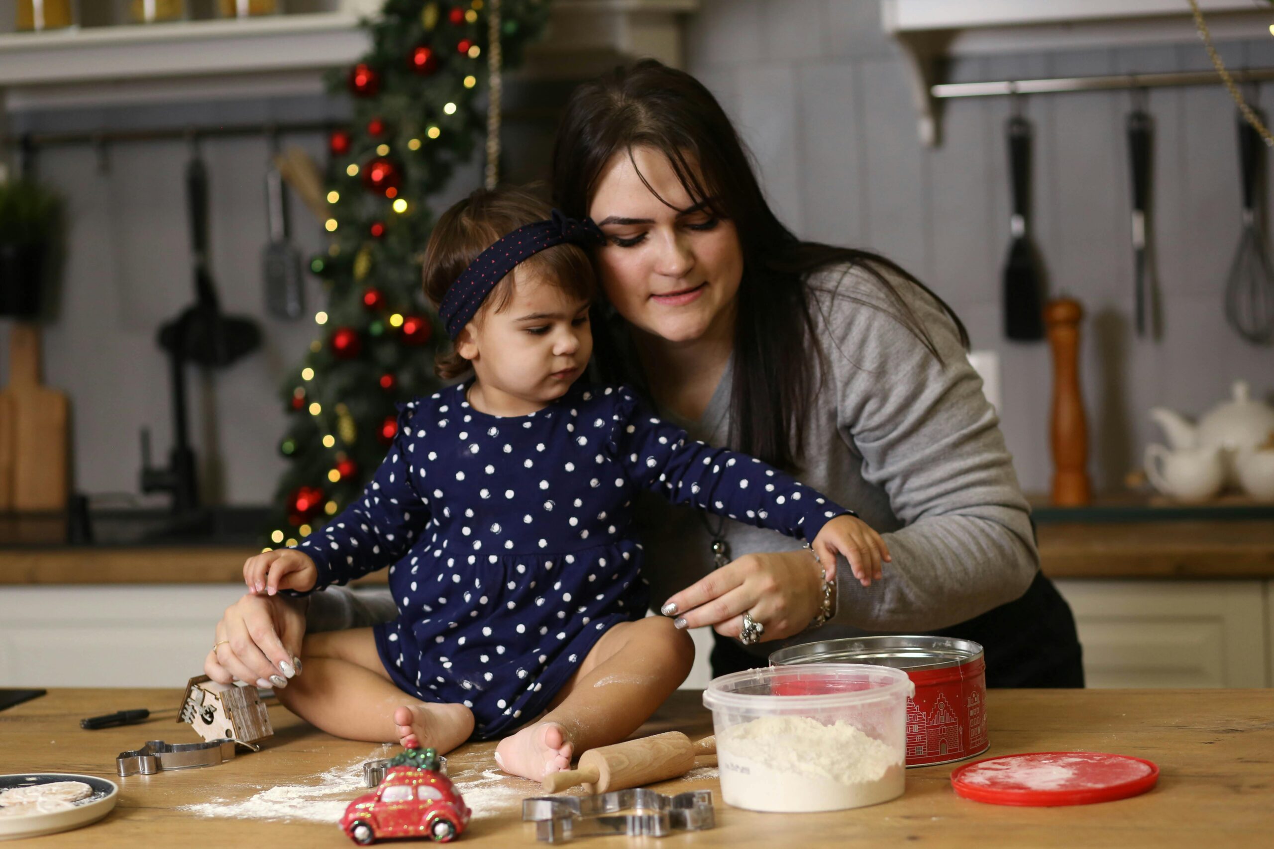 A toddler helping a parent bake Christmas cookies in a warm cozy kitchen.