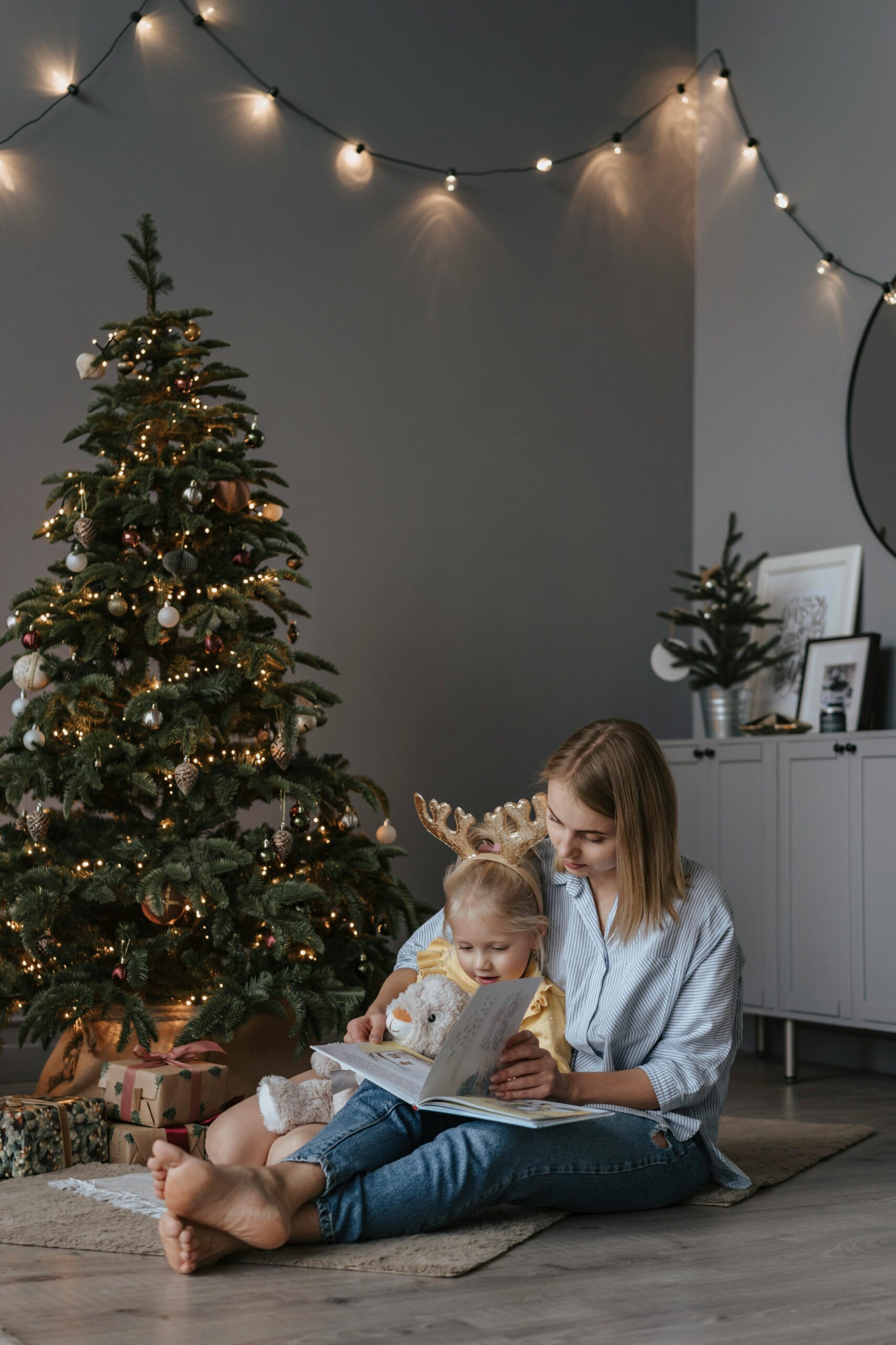 A parent reading a children’s Bible to a child near soft Christmas lights.